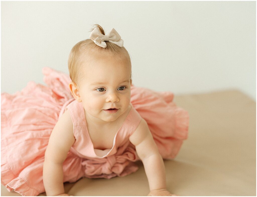 A baby in a pink dress crawls towards a Milwaukee family photographer.