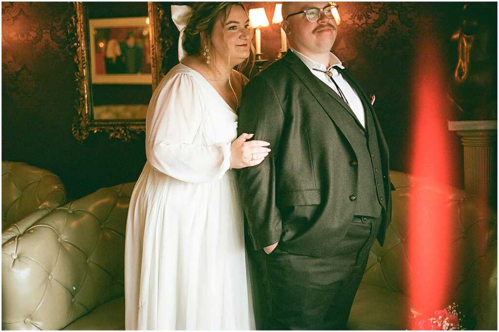 A bride stands behind a groom in a film wedding photo with a light leak.