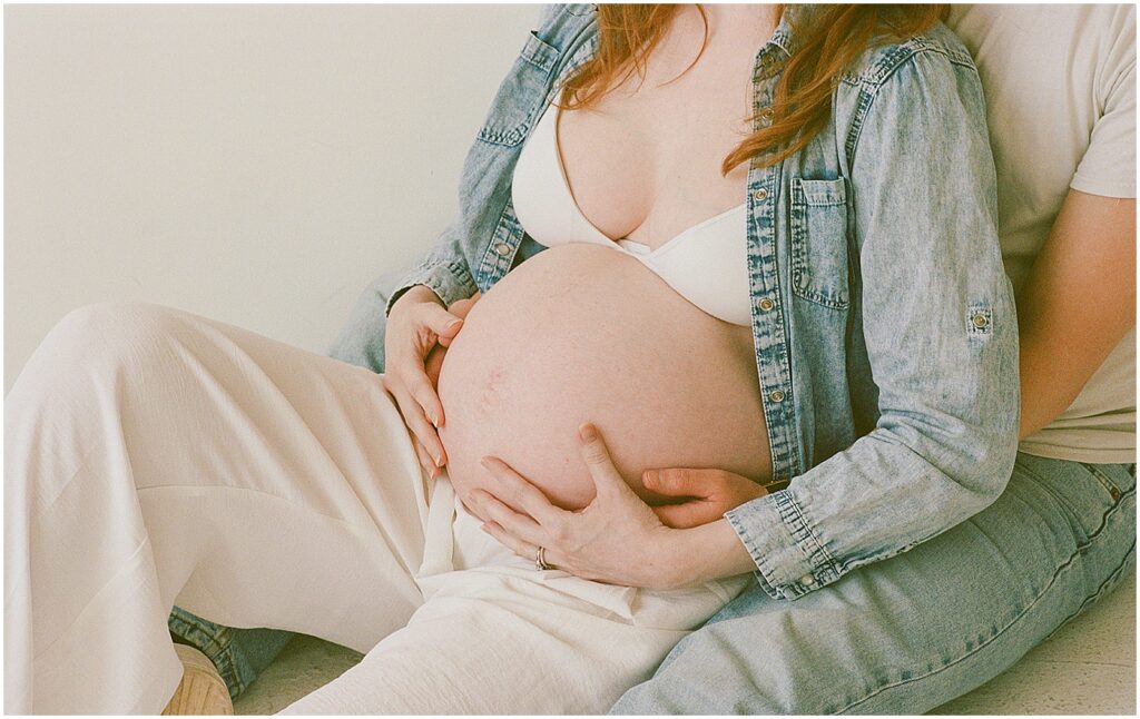 A man sits with his arms around his pregnant wife during a Milwaukee maternity photoshoot.