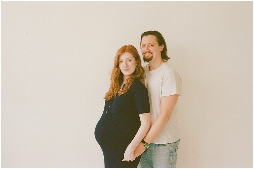 A pregnant woman stands with her back to her husband in a Milwaukee maternity studio.