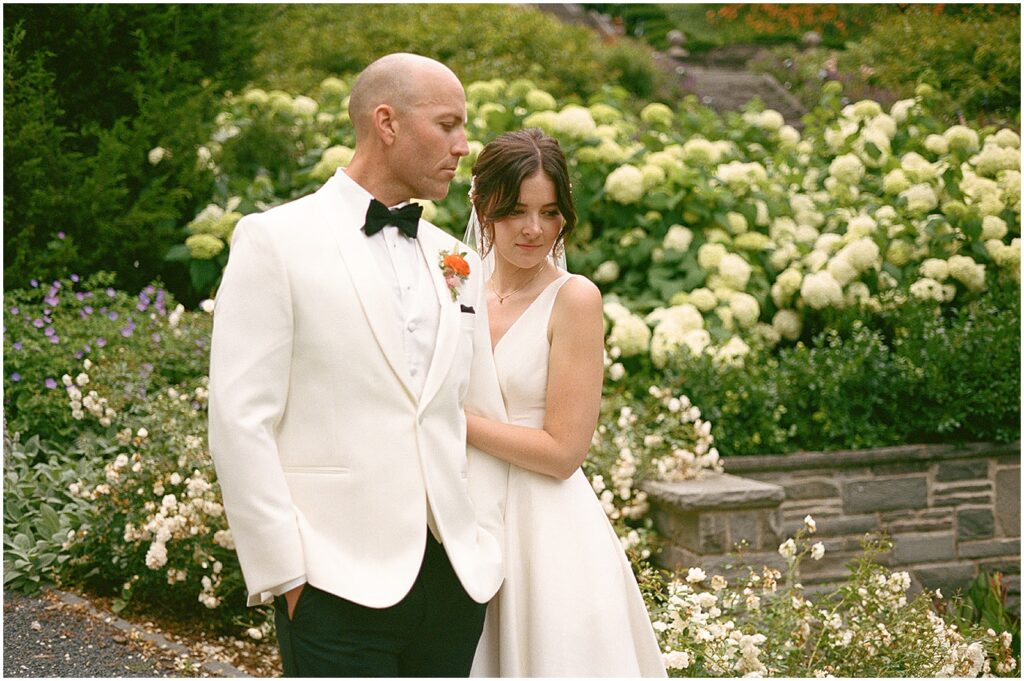 A bride holds a groom's arm in a garden at their art museum Milwaukee wedding.