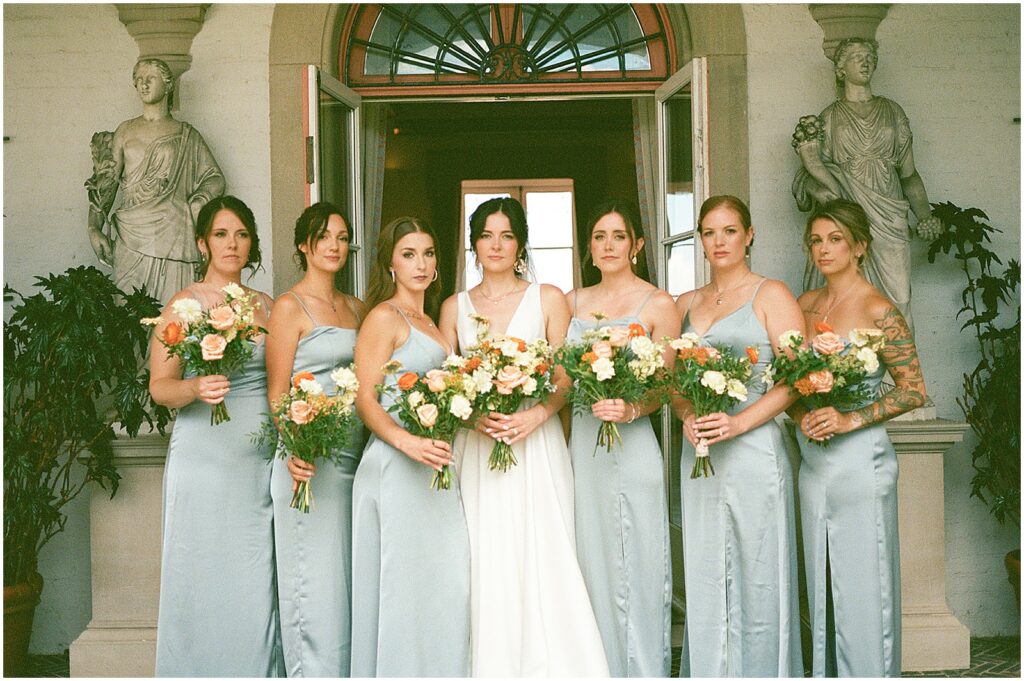 A bride and her bridesmaids pose in front of an art museum doorway at a Milwaukee wedding.