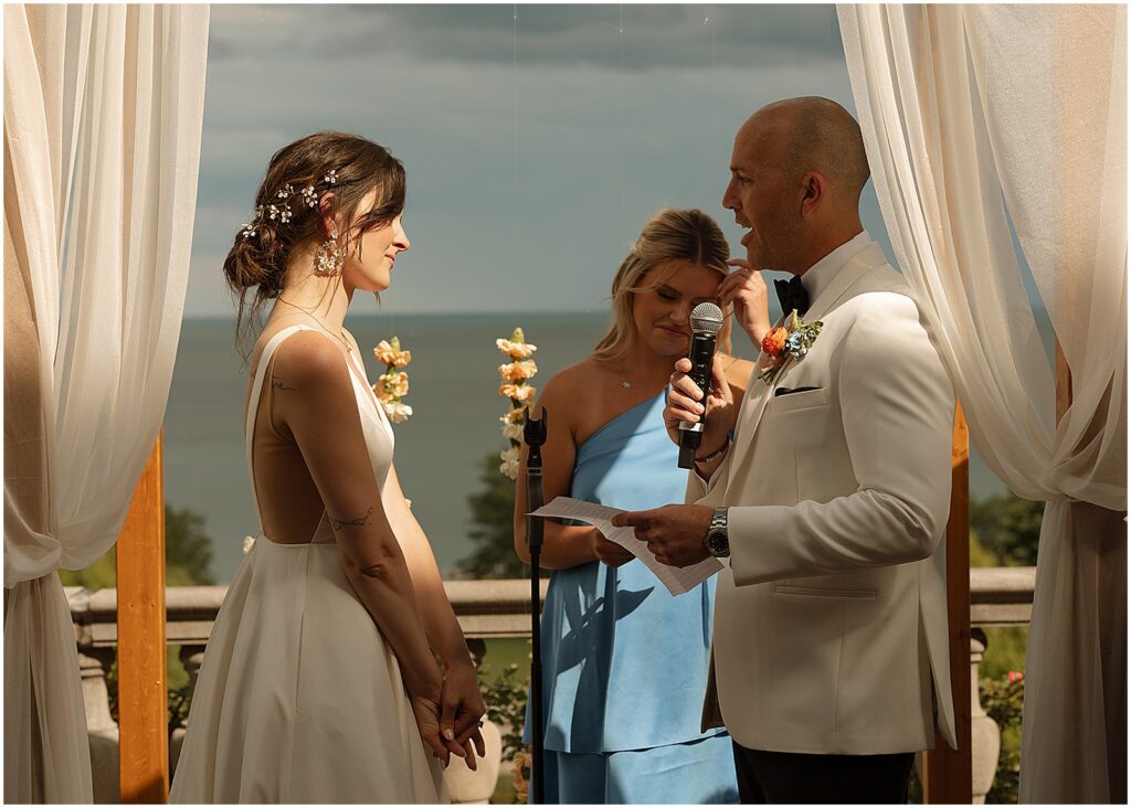 A groom reads his vows under a chuppah made of wood and white cloth.