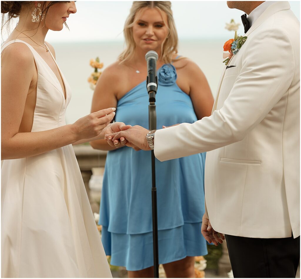 A bride puts a groom's wedding ring on his finger with Lake Michigan in the background.