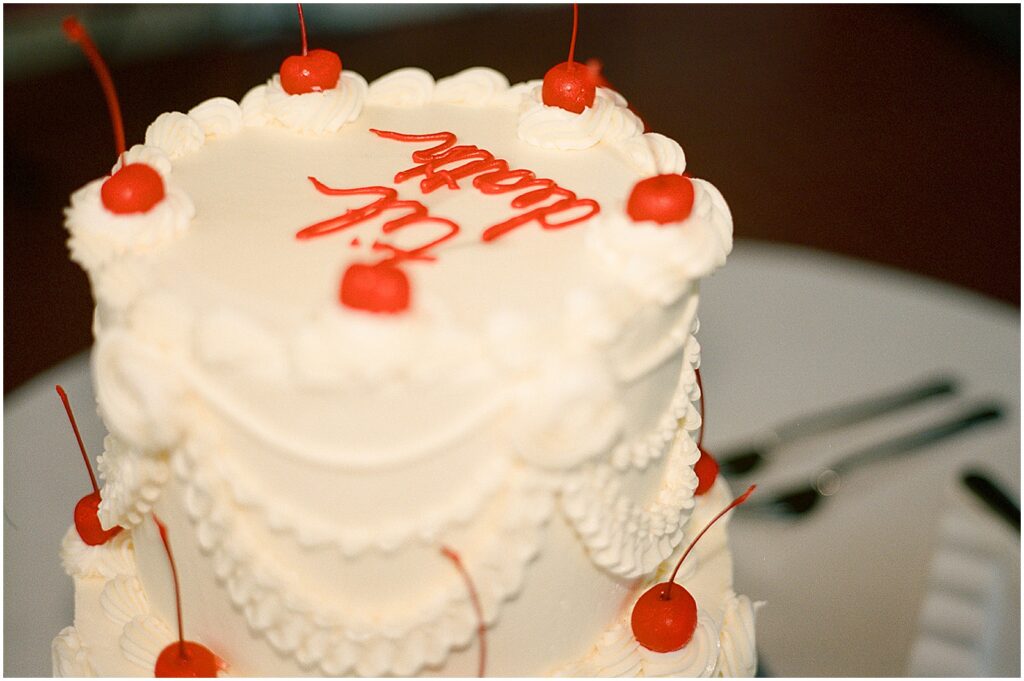 A vintage wedding cake is decorated with cherries and red letters that read "til death."