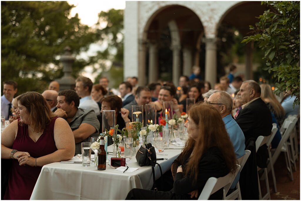 Wedding guests listen to speeches at long reception tables at an art museum wedding venue in Milwaukee.