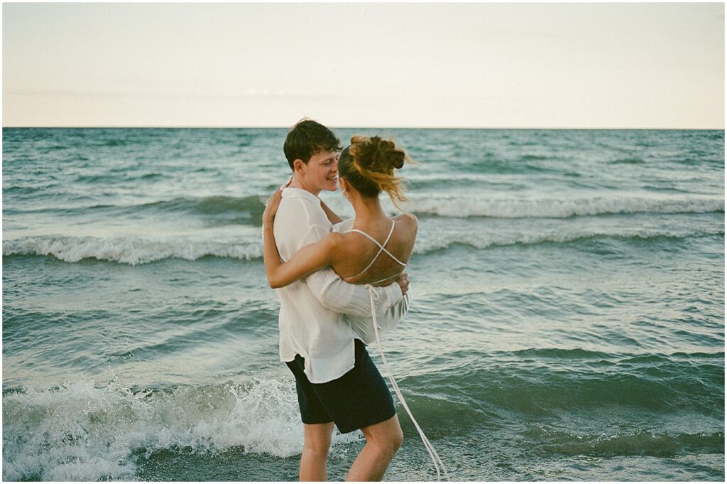 A groom carries a bride along the shore in elopement photos at Atwater Beach.