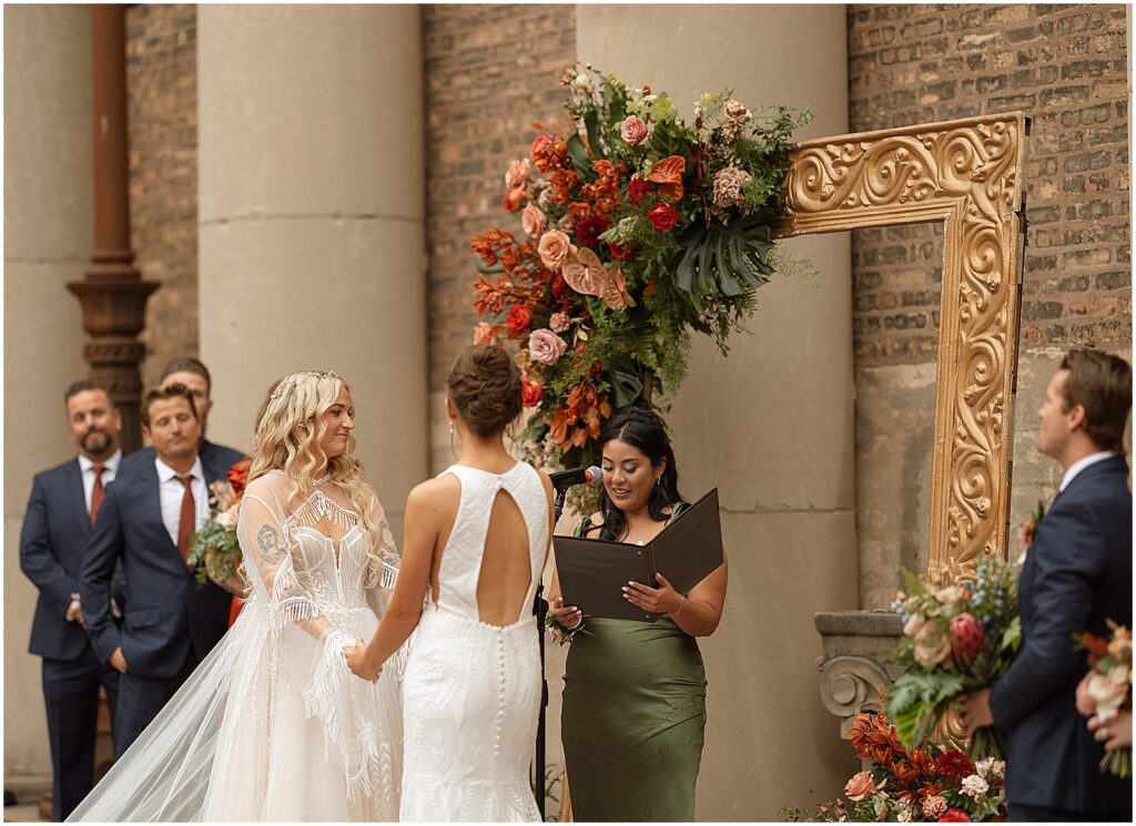 Two brides listen to an officiant read from a wedding ceremony script.