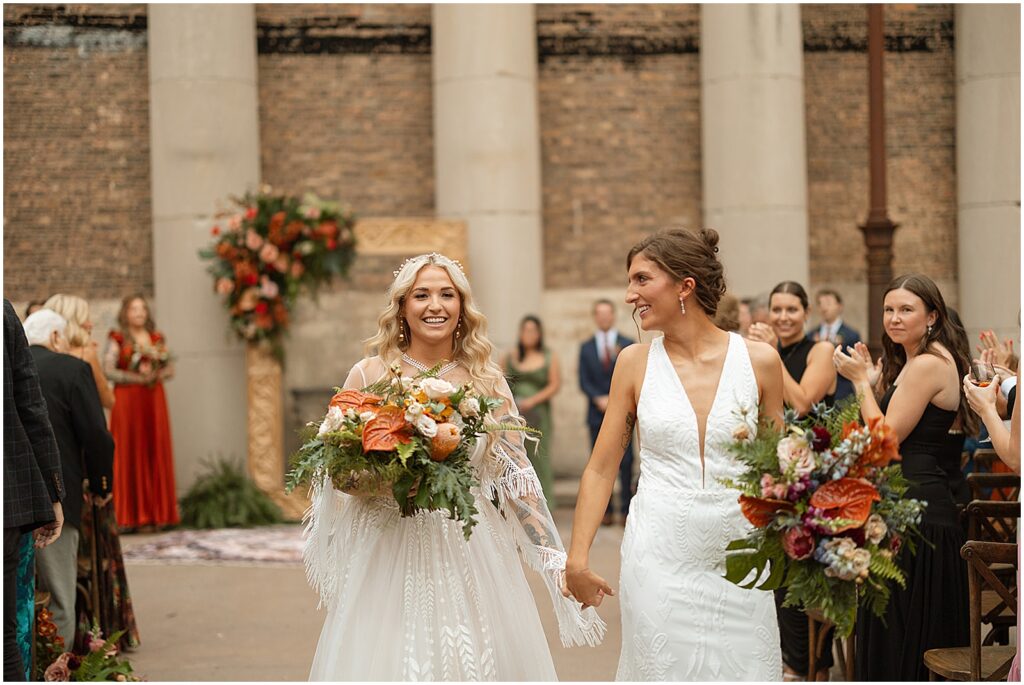 Two brides hold hands during their recessional at their Artifact Events wedding.