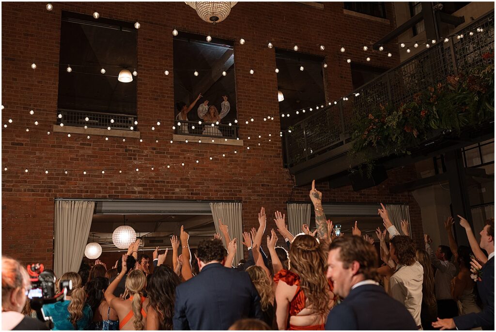 Two brides wave to guests from a mezzanine.