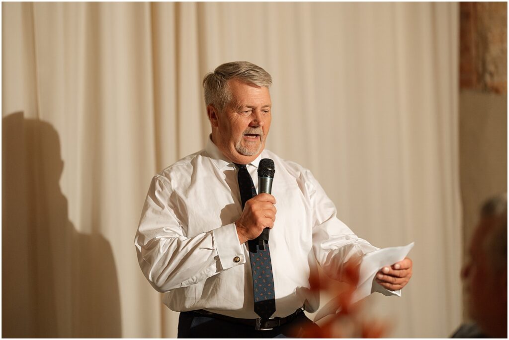 A father of a bride reads a speech from a paper.