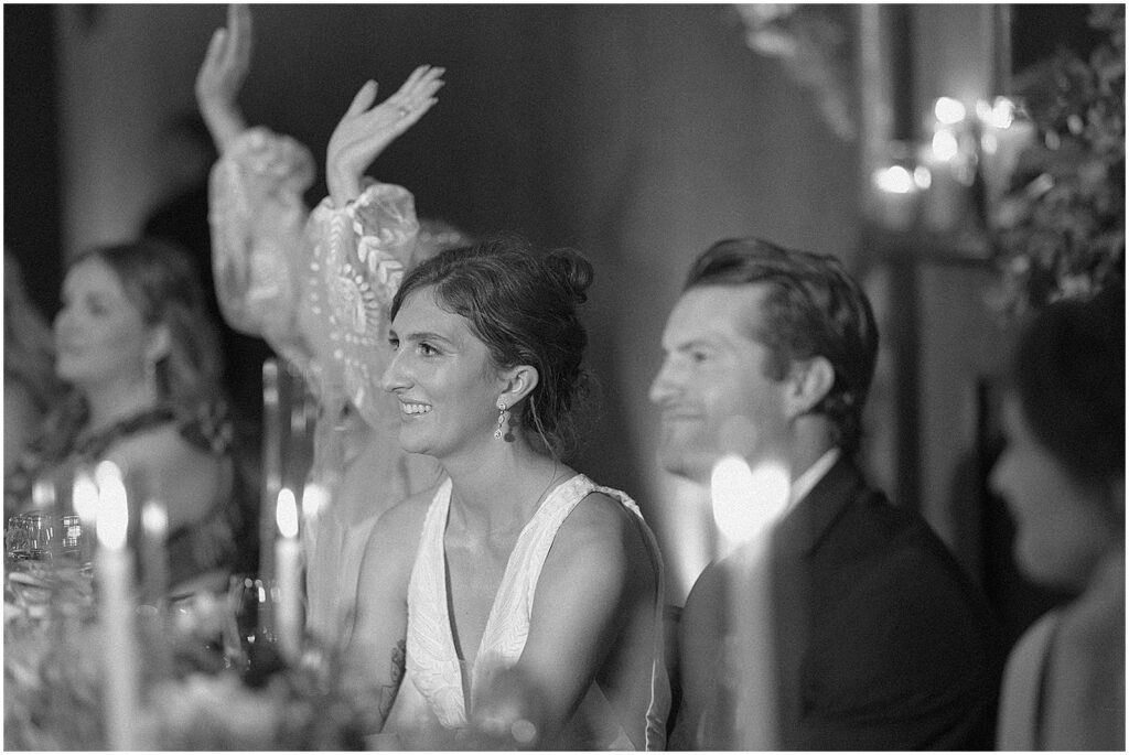 A bride smiles from a table during a wedding toast.