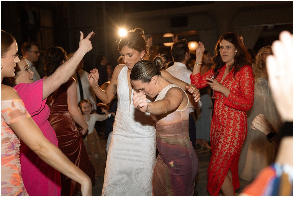 A bride dances with her arm around a wedding guest.