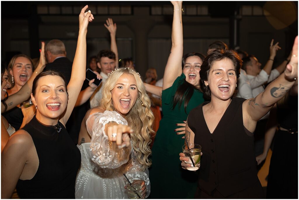 A bride and wedding guests wave to a Midwest wedding photographer on the dance floor.