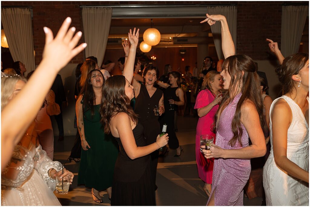 Wedding guests dance with their arms in the air.