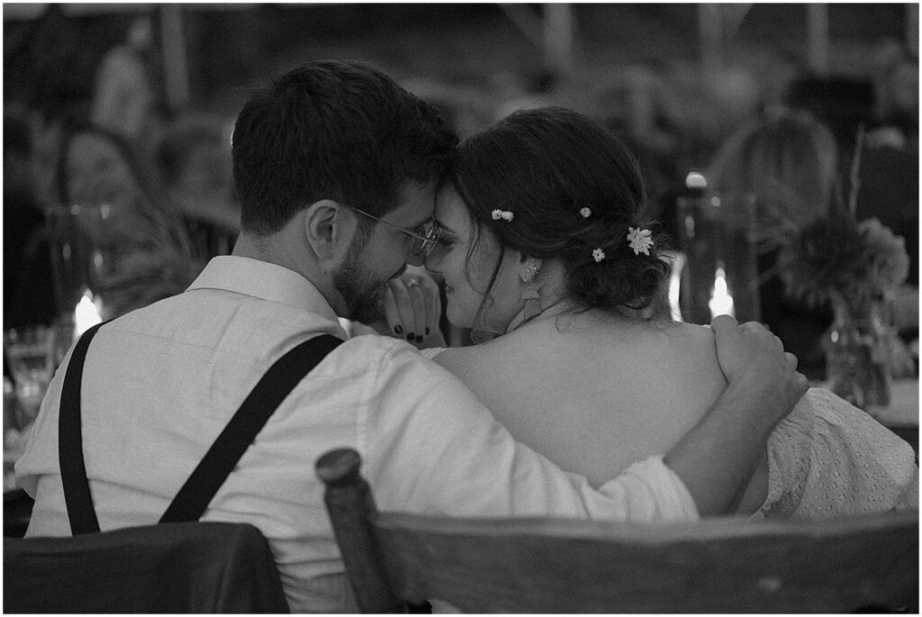 A bride and groom lean towards each other while they listen to a toast.