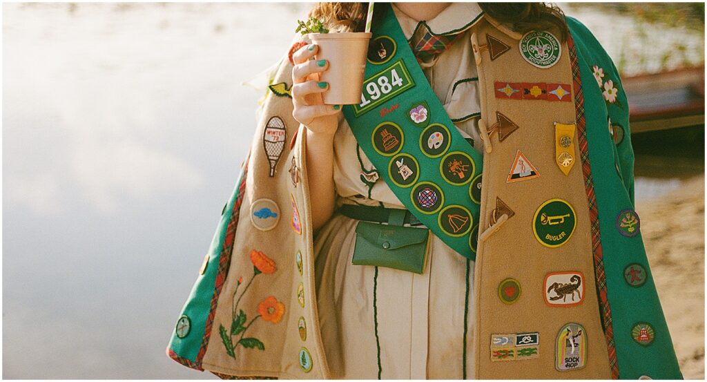 A woman wears a vest covered in merit badges on the beach at Camp Wandawega.