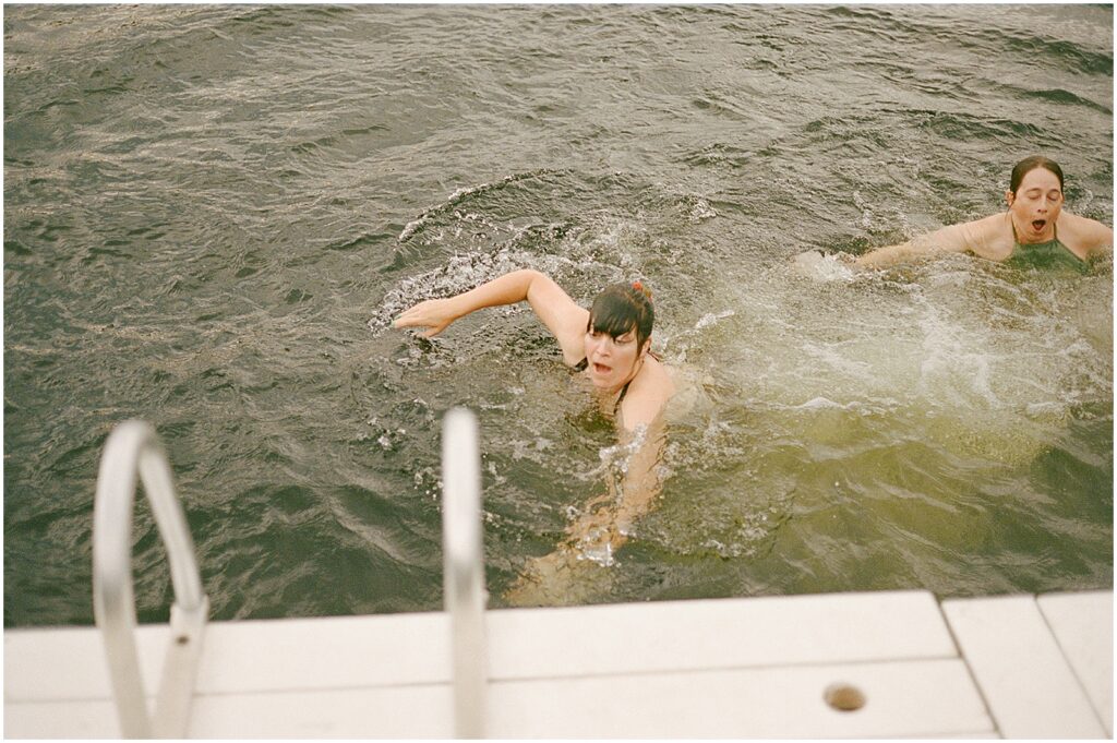 Women swim towards a ladder on a dock.