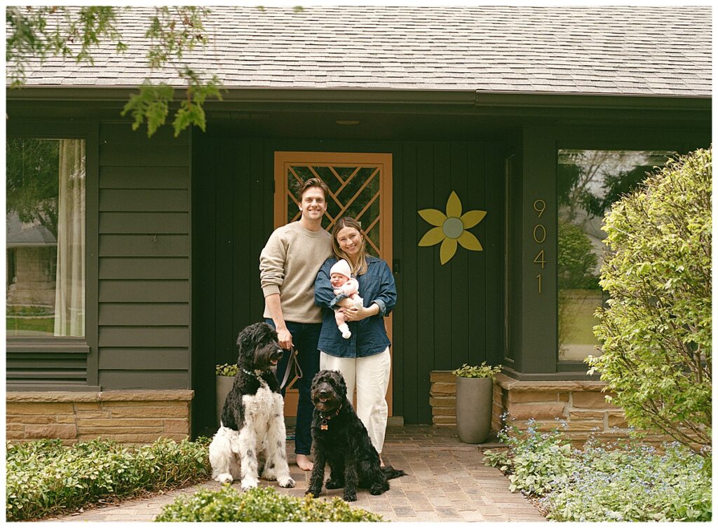 couple standing in front of their home with their newborn
